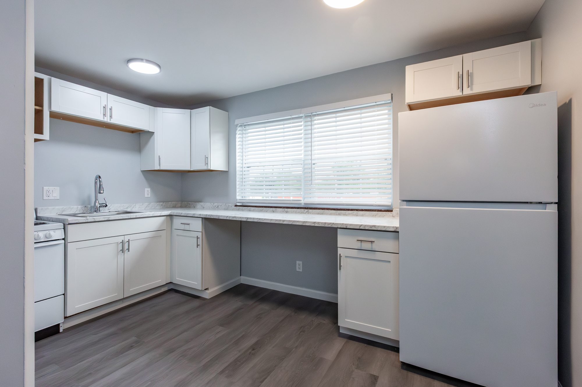Renovated apartment kitchen with white shaker cabinets, full-size refrigerator, and a sunny window counter at Cleve Royale Apartments