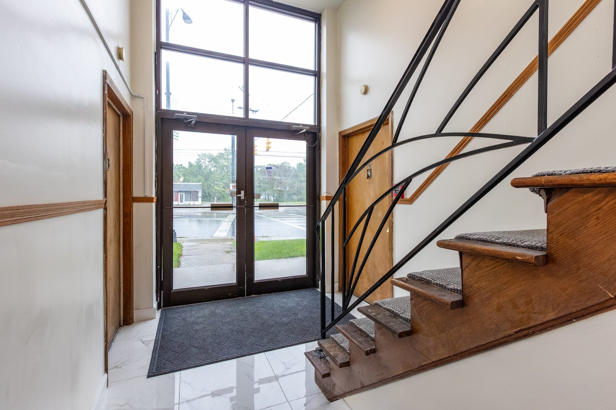 Bright entry lobby with glass doors and a classic wood staircase at Cleve Royale Apartments on Cleveland Ave in Columbus, OH
