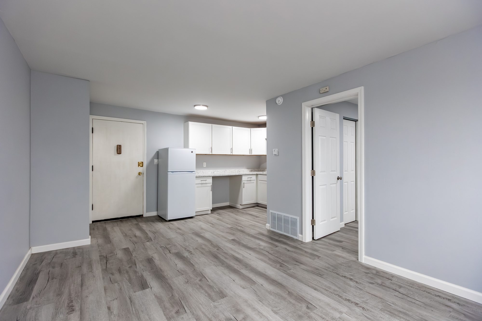 Bright, open living area with wood-look flooring and an updated kitchen in a newly renovated Cleve Royale apartment