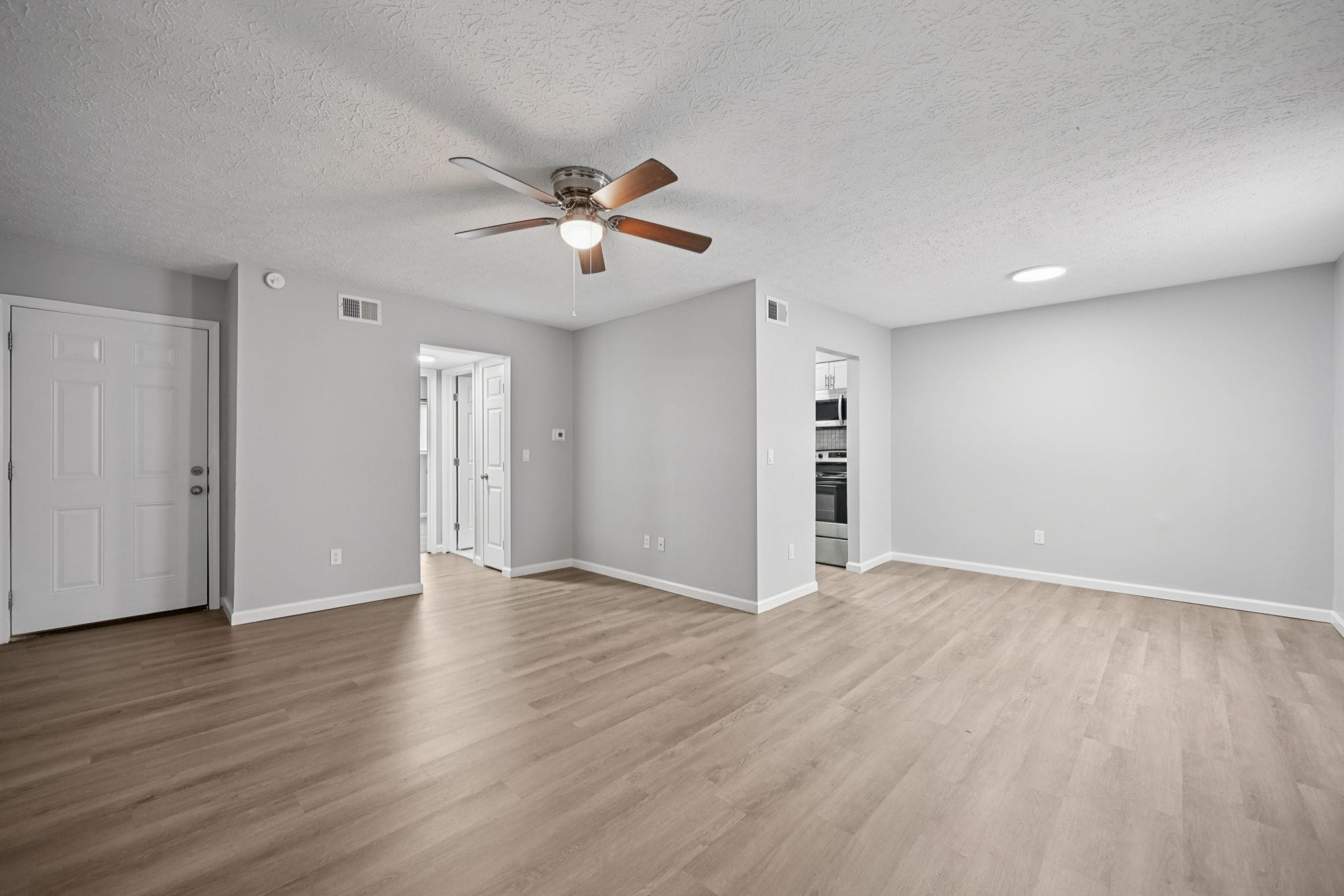 Bright, open living room with ceiling fan and wood-look flooring in a newly renovated Cleve Royale apartment